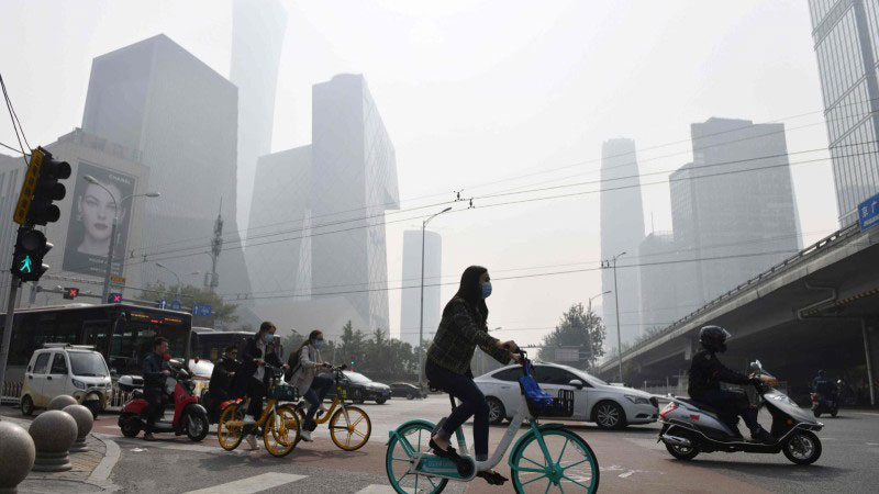 Des cyclistes traversant une route un jour de pollution à Pékin, en octobre 2020. Le pays veut parvenir à la neutralité carbone en 2060. (photo AFP)