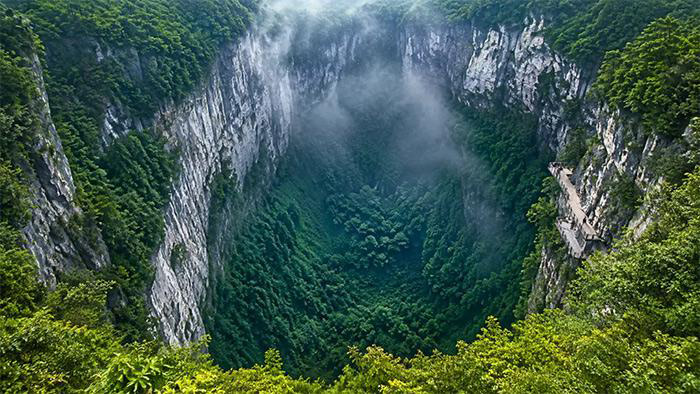 Le gouffre Xiaozhai Tiankeng, dans la région de Chongqing, abrite une forêt subtropicale ancienne protégée par un microclimat unique – DailyGeekShow.com / Image Illustration
